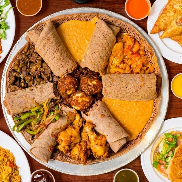 Overhead view of a large platter of Ethiopian injera with various stews, surrounded by other dishes.