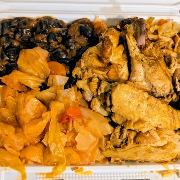 A takeout container filled with seasoned chicken, black beans, and stewed cabbage on a dark counter.