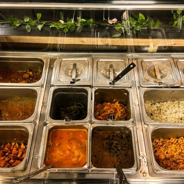 A buffet line with various dishes in metal trays, including rice, beans, and stews.